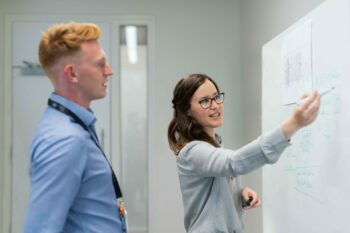 Woman explaining how angel investment networks work on a whiteboard to a colleague.