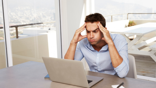 Man with head in hands looking at laptop