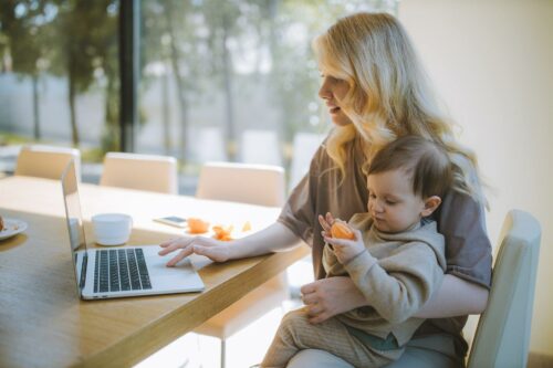 Woman on laptop holding child, trying to get a grasp on her worklife balance