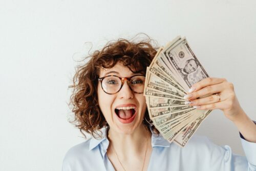 woman with curly hair and glasses holding the money like a fan, after receiving great R&D tax advice