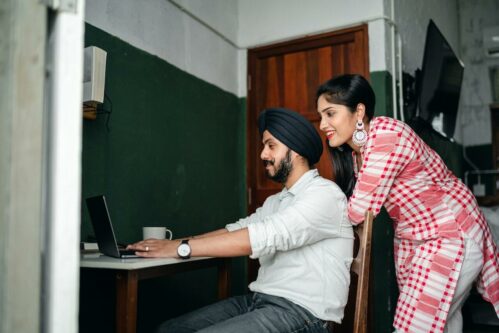 Young Indian woman helping husband working on laptop on remote project